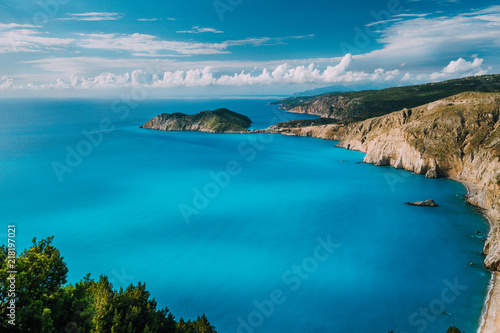 View of Kefalonia west coastline. Assos village town and Frourio peninsular. Beautiful milky blue bay with brown rocky limestone costline and moving white clouds on horizon. Greece