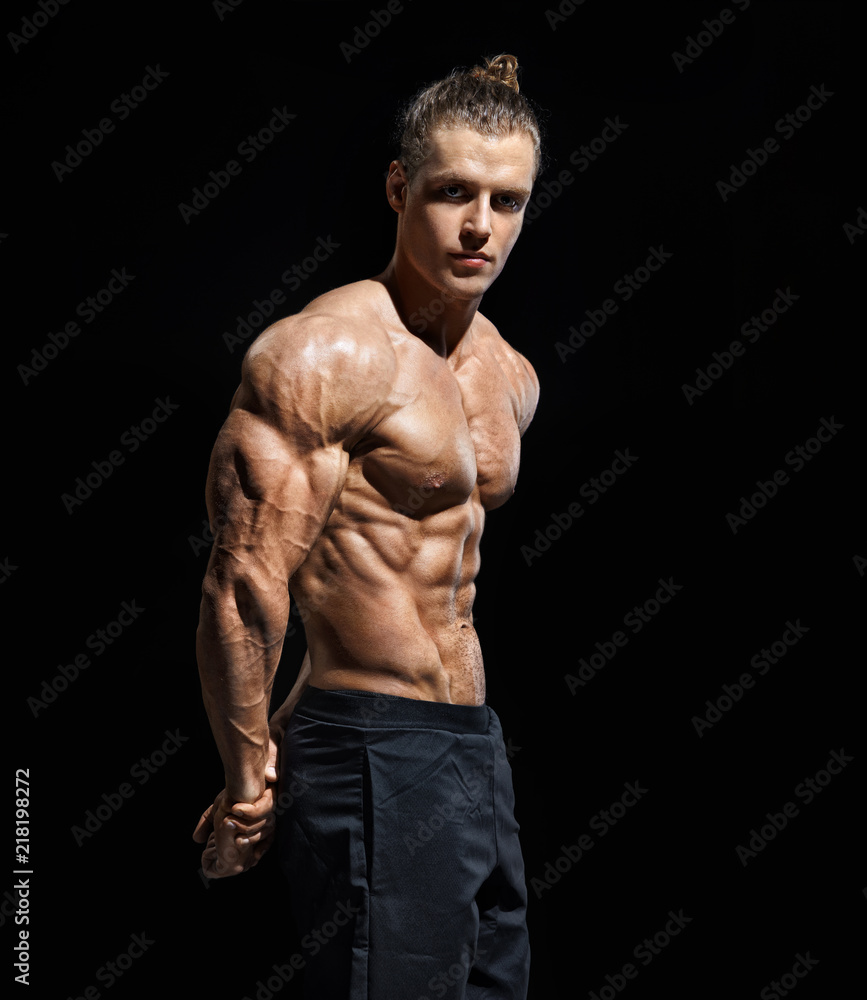 Fototapeta premium Strong athletic man posing. Photo of man with perfect physique after training on black background. Strength and motivation
