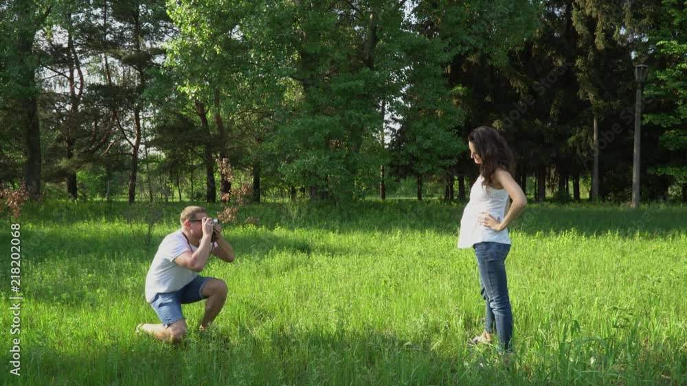 Handsome man takes photos with camera of young happy pregnant woman in park Handsome man takes photos with camera of young happy pregnant woman in park