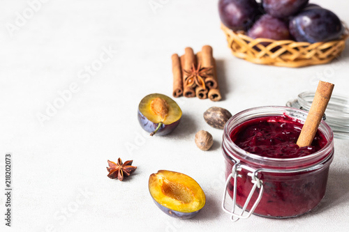 Homemade plum jam with spices (anise, cinnamon) and fresh plum on a white background.