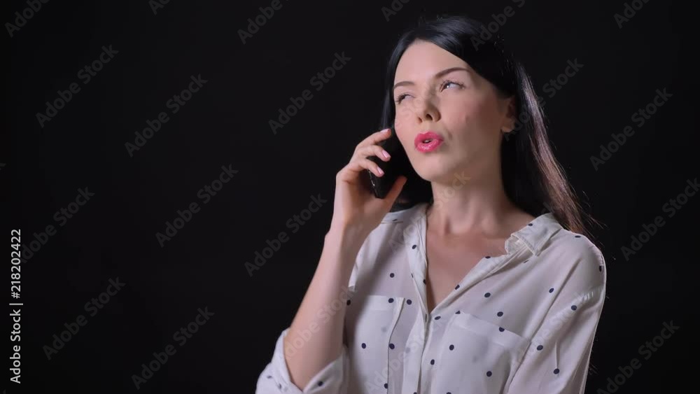 Gorgeous pensive young brunette woman talking on phone, standing isolated on black background Gorgeous pensive young brunette woman talking on phone, standing isolated on black background