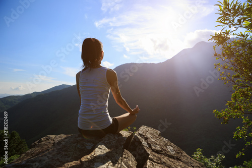 Yoga woman meditating on mountain peak cliff edge in the sunrise