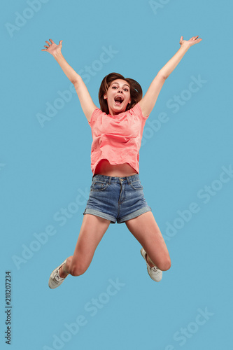 Freedom in moving. Mid-air shot of pretty happy young woman jumping and gesturing against blue studio background. Runnin girl in motion or movement. Human emotions and facial expressions concept