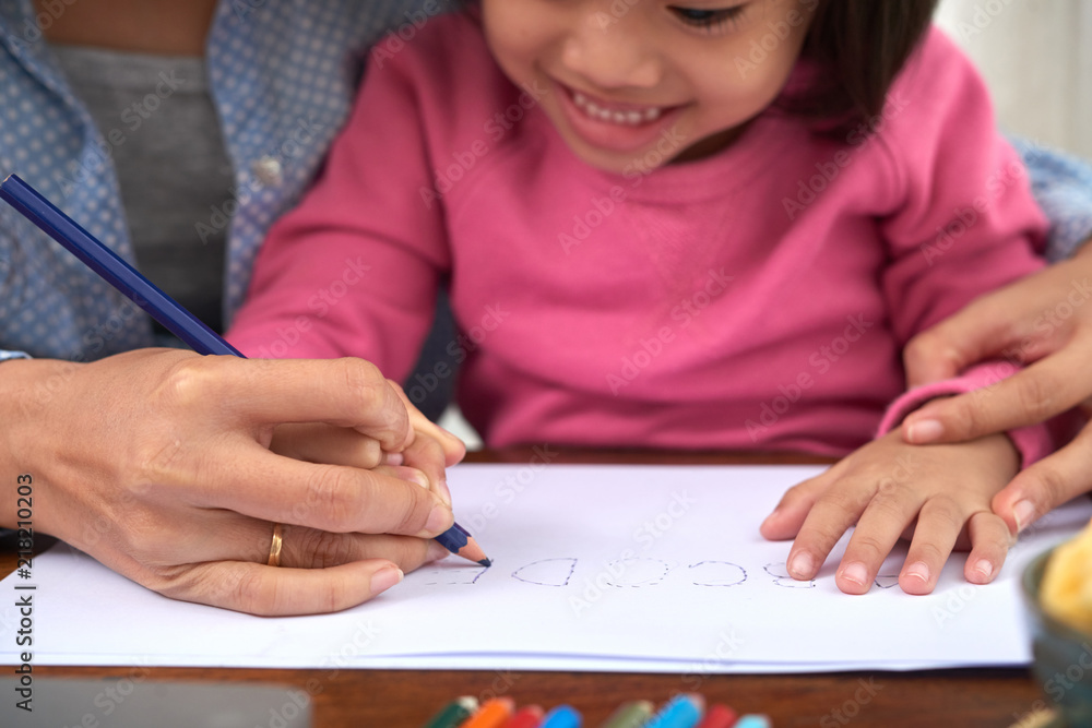 Corp woman helping little Asian girl drawing alphabet on paper with colored pencils spending time together Corp woman helping little Asian girl drawing alphabet on paper with colored pencils spending time together