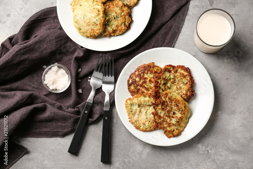 Plates with zucchini pancakes and glass of milk on table