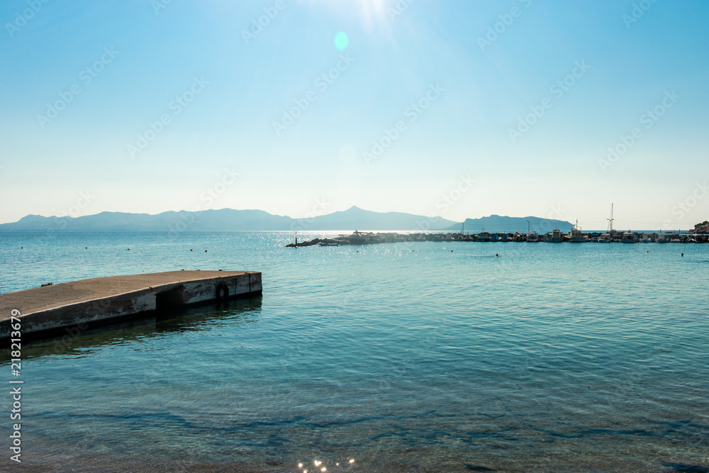 Very blue, peaceful water with mountain in the distance and a pier in the front, tropical