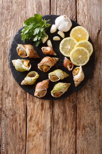Buccinum undatum, the common whelk, sea snails with a garlic and parsley, lemon close-up. Vertical top view from above