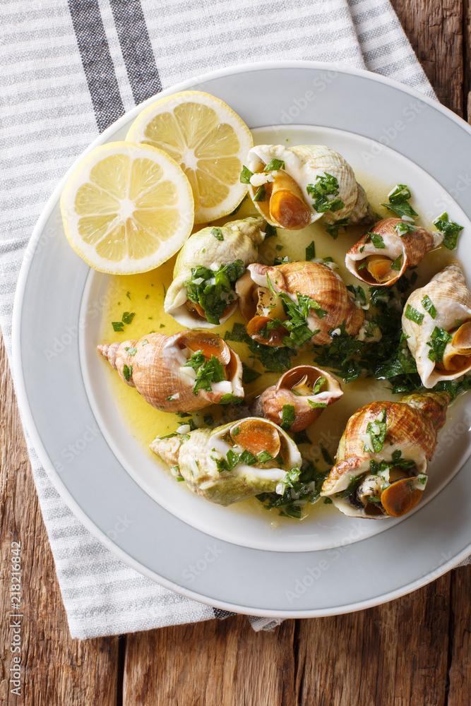 French shellfish bulot whelks served with a sauce of butter, garlic and parsley, lemon close-up. Vertical top view from above French shellfish bulot whelks served with a sauce of butter, garlic and parsley, lemon close-up. Vertical top view from above