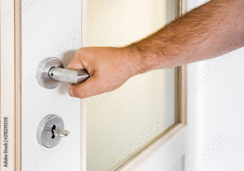 Hand holds doorknob on wooden door with glass