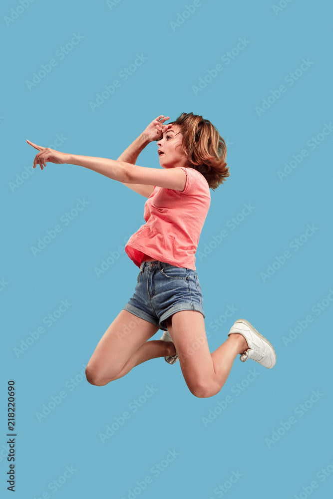 Freedom in moving. Mid-air shot of pretty happy young woman jumping and pointing by finger against blue studio background. Runnin girl in motion or movement. Human emotions and facial expressions Freedom in moving. Mid-air shot of pretty happy young woman jumping and pointing by finger against blue studio background. Runnin girl in motion or movement. Human emotions and facial expressions