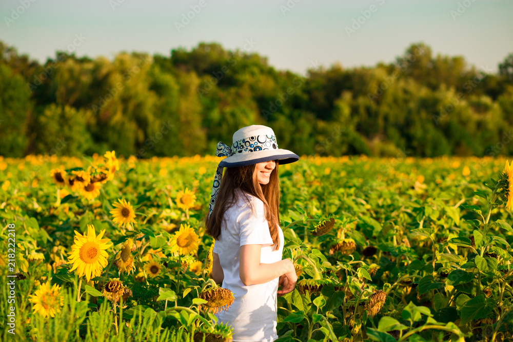 Summer portrait of happy young woman in hat with long hair in sunflower field enjoying nature