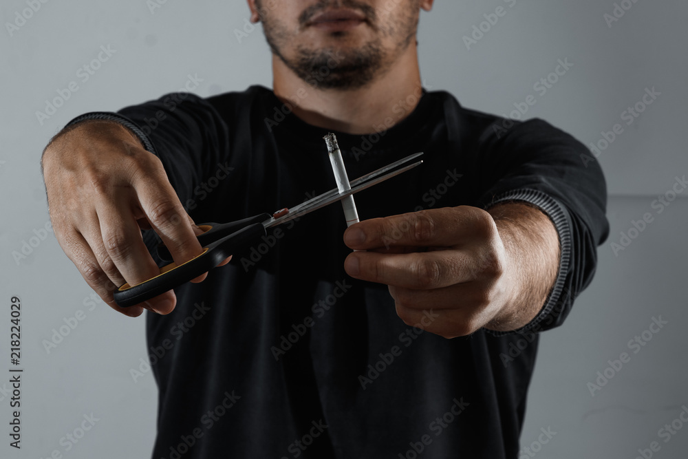 Fotografie The man on a dark background cuts the cigarette with scissors