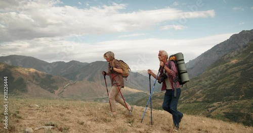Active senior caucasian couple hiking in mountains with backpacks, enjoying their adventure 4k