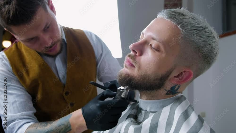Shaving of beard. Barber cutting men's face hair with beard trimmer at