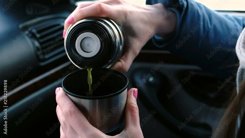 Close-up woman's hands pouring a hot tea in a cup from thermos in the car in winter. Close-up woman's hands pouring a hot tea in a cup from thermos in the car in winter.