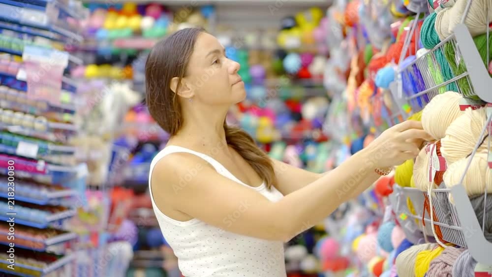 A young woman chooses yarn for knitting clothes at the Mall. No visible trademarks or logos. The average shot with the shelves in the background. A young woman chooses yarn for knitting clothes at the Mall. No visible trademarks or logos. The average shot with the shelves in the background.