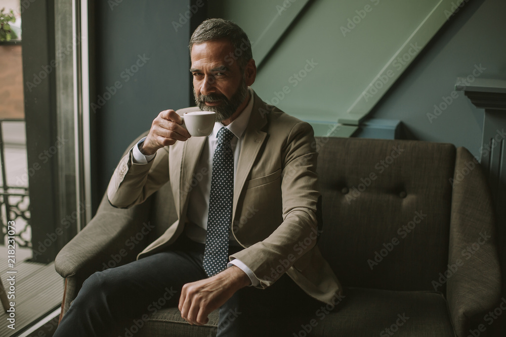 Handsome elegant serious businessman sitting in armchair and holding cup of espresso. Handsome elegant serious businessman sitting in armchair and holding cup of espresso.