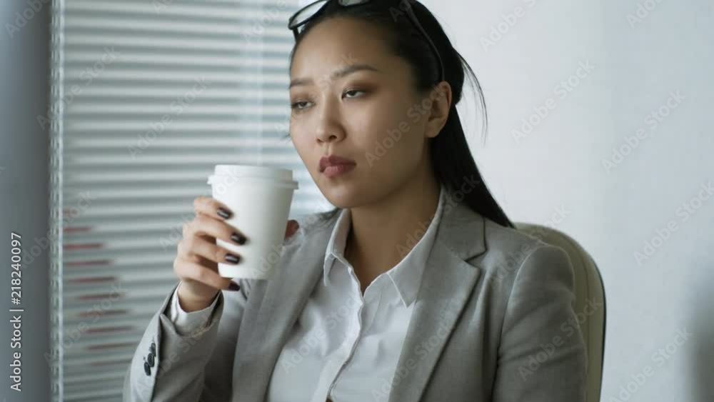 Medium shot of tired Asian businesswoman taking off glasses and drinking takeaway coffee when taking break from work in office Medium shot of tired Asian businesswoman taking off glasses and drinking takeaway coffee when taking break from work in office
