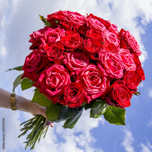 female hand holds a bouquet of red roses against the blue sky