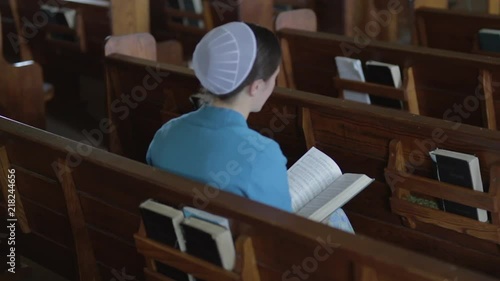 A Mennonite woman sits in an empty church pew and flips through a hymnal.