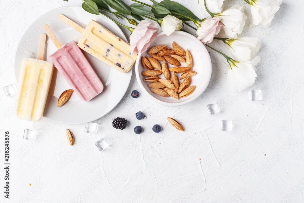 Homemade frozen ice cream popsicles from fruits and berries on table whith flowers and ingridients, top view