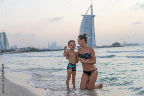 Portrait smiling little baby boy playing and mother in the sea, ocean. Positive human emotions, feelings, joy. Funny cute child making vacations and enjoying summer. Sunset Dubai beach.