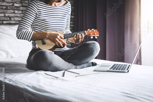 Young happiness woman on bedroom in enjoying playing the music with guitar or ukulele in holiday, relaxation and recreation concept photo