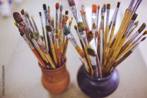 A bunch of art brushes standing in ceramic vases, on the table in the art studio