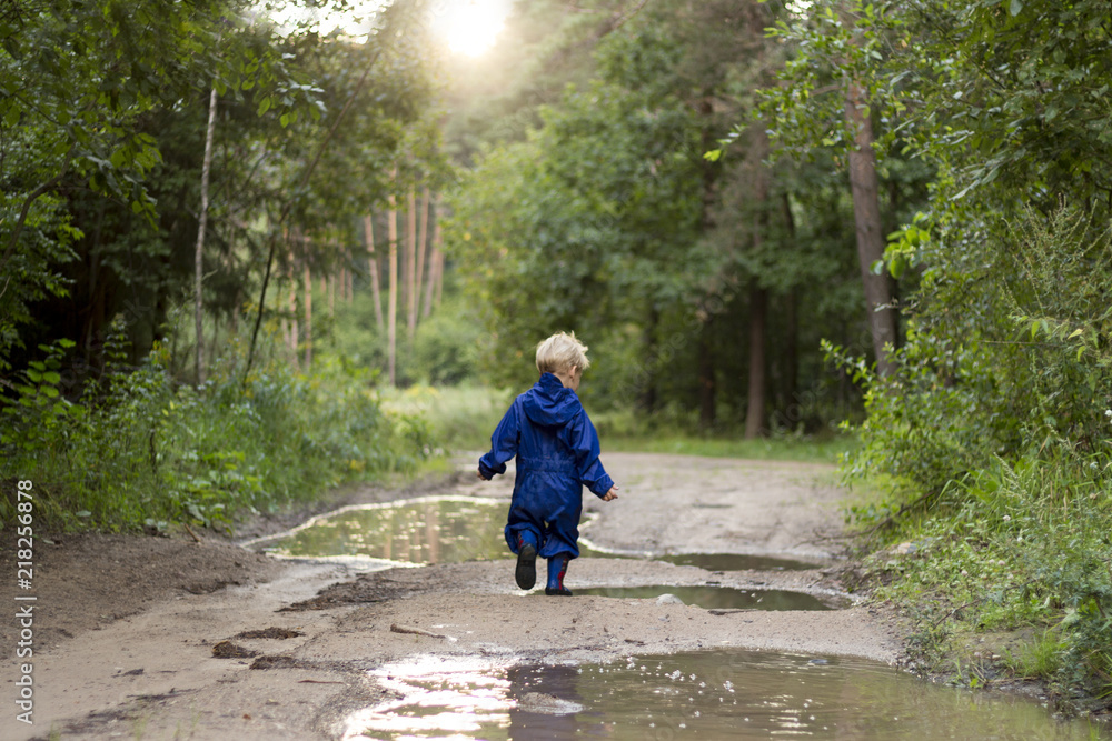 Baby boy walking in the forest. 2 years kid running through puddles