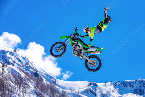Fotografie racer on a motorcycle in flight, jumps and takes off on a springboard against th