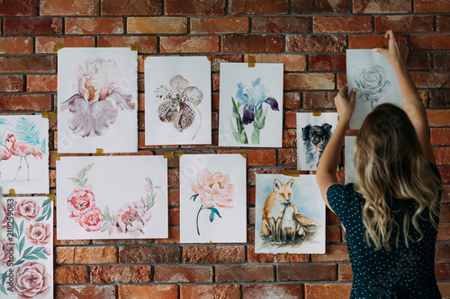 art studio workspace. painter artwork. woman sticking watercolor drawings of flowers and animals to the wall