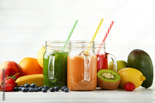 Sweet smoothie in glass jars with fruits on white wooden table