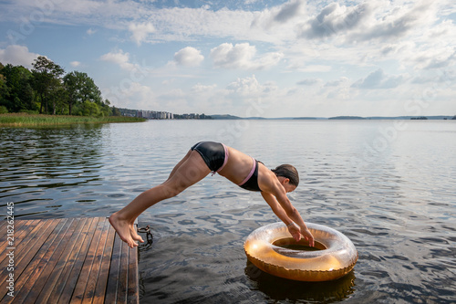 Canvas Print Side view of one young girl diving into water and svim ring from a jetty at a summer lake
