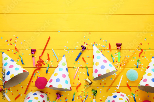 Birthday paper caps with candles and blowers on yellow wooden table