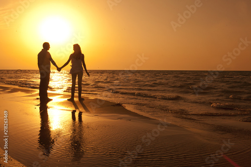 Love couple silhouette walking in the beach in summer sunset