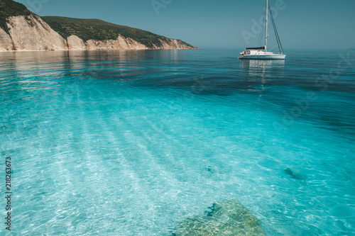 Fotografia Azure blue lagoon with calm waves and drift sailing catamaran yacht boat