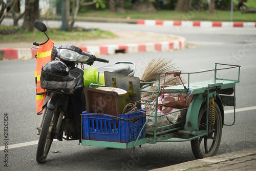 Phuket, Thailand - 10 August 2018- sidecar 's cleaner with broom, black helmet in basket, reflective clothing  hang on the mirror, scales and rope in blue plastic basket photo