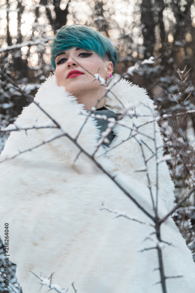 A nice girl with blue hair wrapped in a white fur coat in a snow-covered park posing and laughing. Portrait of a cheerful girl on a bush background A nice girl with blue hair wrapped in a white fur coat in a snow-covered park posing and laughing. Portrait of a cheerful girl on a bush background