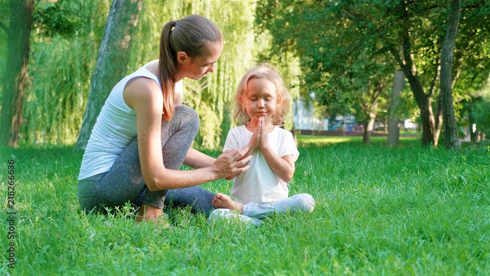 Fototapeta premium Young sporty mother coaching her little cute daughter doing yoga exercise