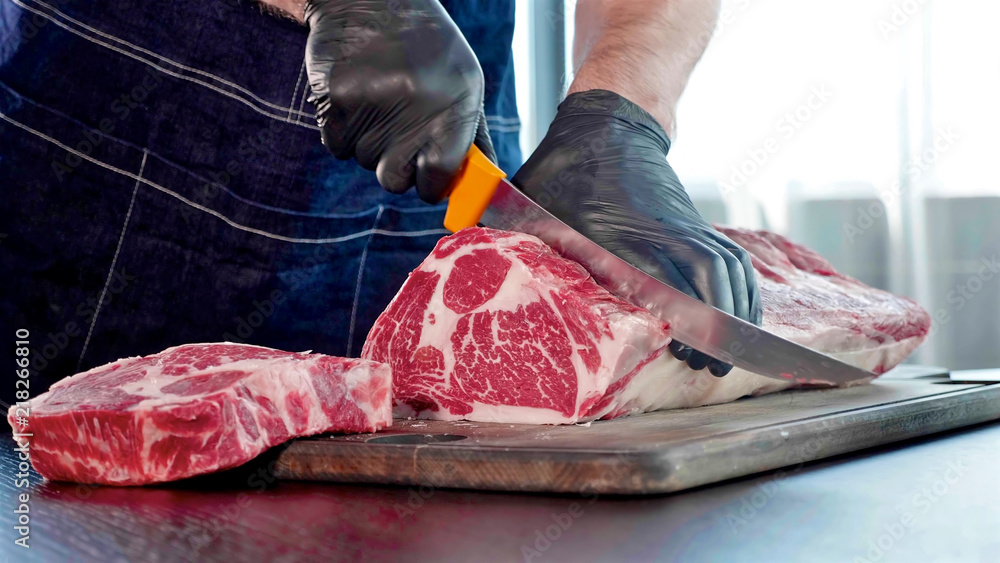 Chef cuts raw meat on the wood board with the knife, close-up