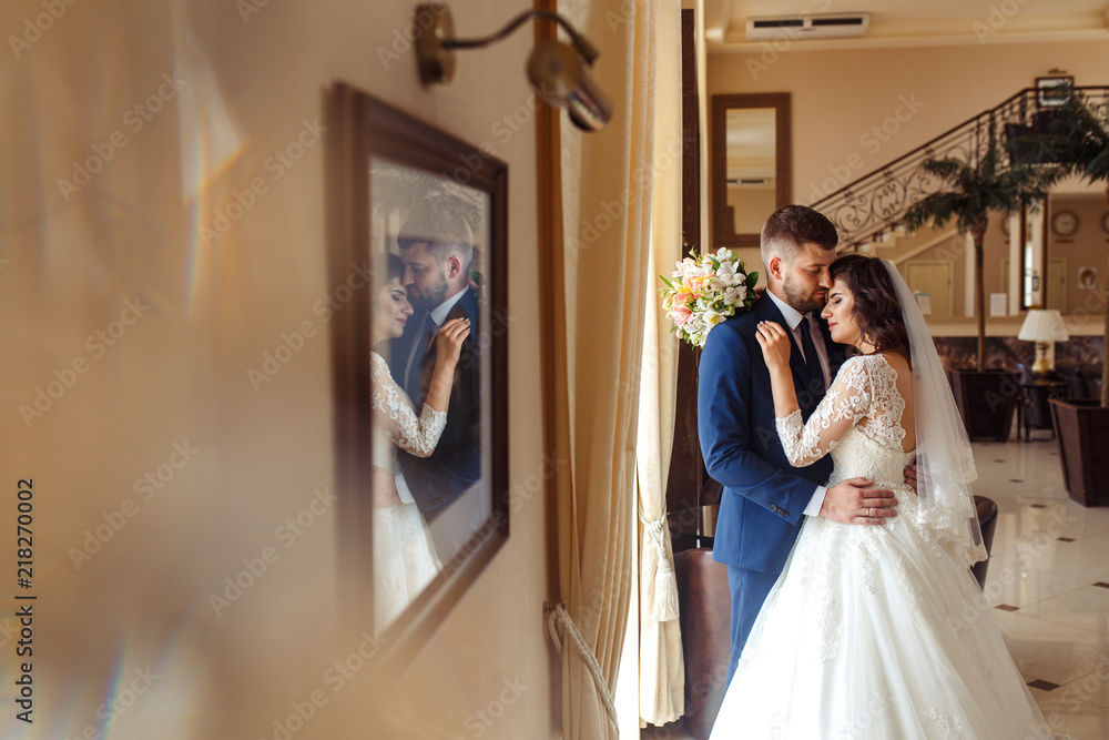 Fototapeta premium Beautiful Bride and Groom enjoy each other in the nice hall of the hotel. happy romantic young couple celebrating their marriage.Sexy kissing stylish couple of lovers close up portrait. wedding