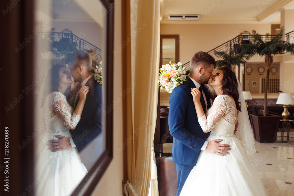 Fototapeta premium Beautiful Bride and Groom enjoy each other in the nice hall of the hotel. happy romantic young couple celebrating their marriage.Sexy kissing stylish couple of lovers close up portrait. wedding
