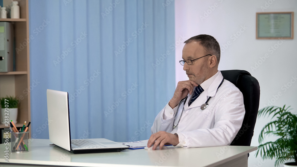 Pensive doctor conducting online consultation for patient, working on laptop