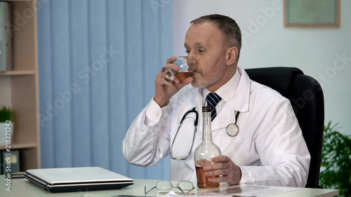 Irresponsible doctor drinking alcohol to relax at work, stressful occupation photo