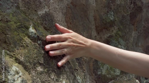 Woman sliding hand against old ancient stone wall in slow motion. Female hand touching hard rough surface of rock with green mold on it