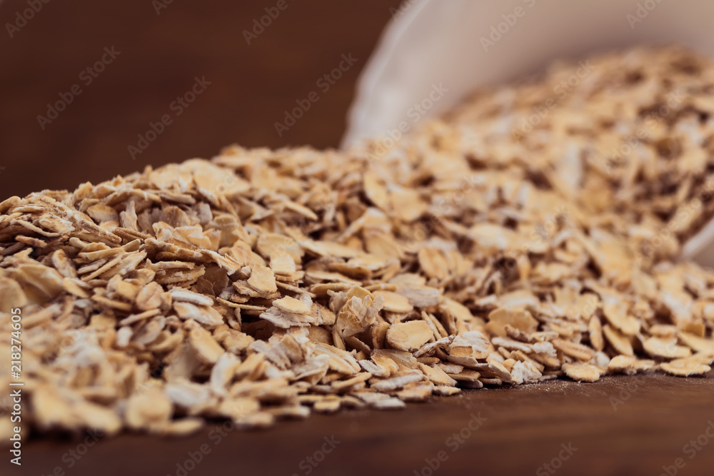 Obraz premium Oat flakes spilled out of a white porcelain bowl on the table, close-up, wooden background.