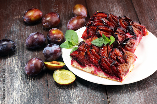 Rustic plum cake on wooden background with plums around.