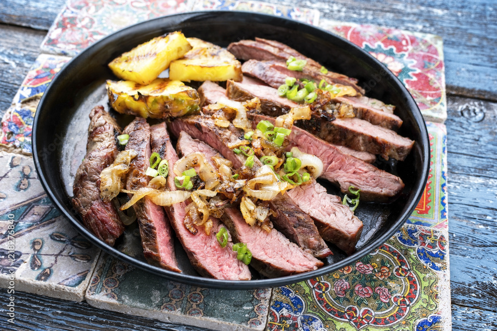 Barbecue dry aged wagyu flank steak with pineapples and onion rings as closeup on a plate Barbecue dry aged wagyu flank steak with pineapples and onion rings as closeup on a plate