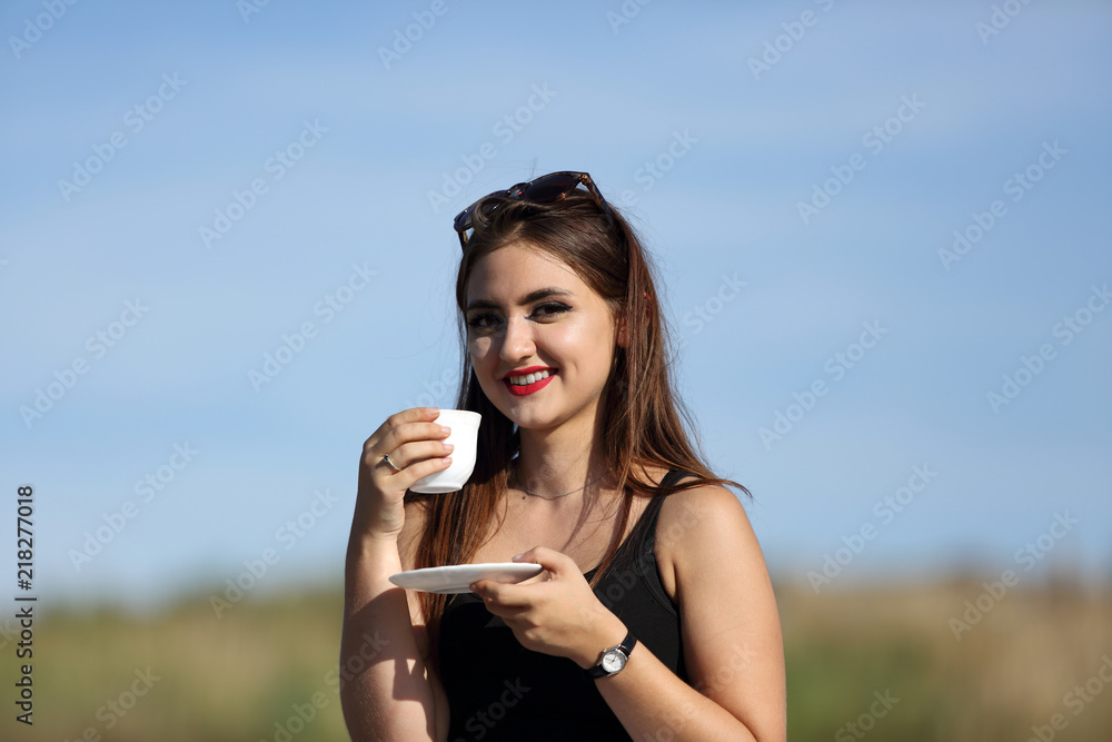 Piękna uśmiechnięta dziewczyna pije kawę z białej filiżanki. - obrazy, fototapety, plakaty 