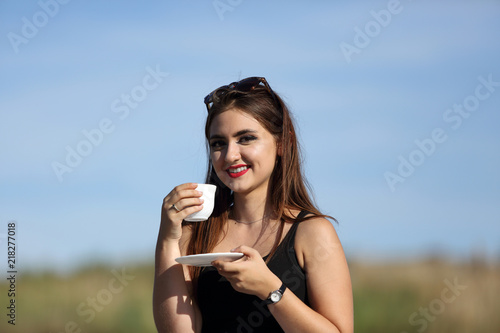 Piękna uśmiechnięta dziewczyna pije kawę z białej filiżanki.